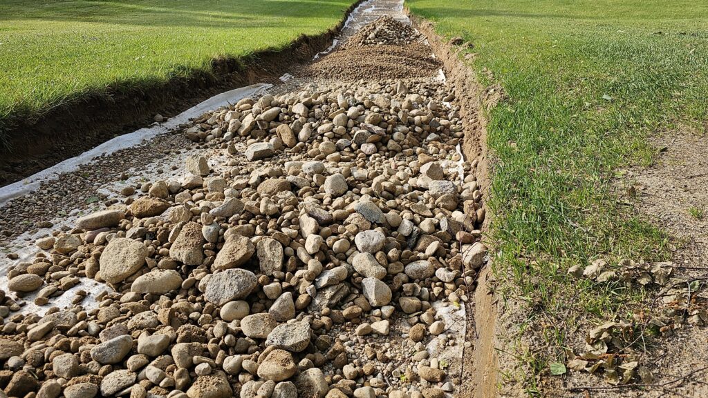 rocky pathway under construction in a green field near a residential area with visible soil and gravel concept